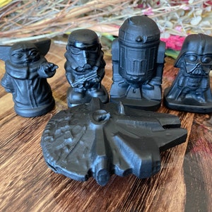 May include: A collection of black Star Wars figurines, including Yoda, a Stormtrooper, R2-D2, Darth Vader, and the Millennium Falcon. The figurines are arranged on a wooden surface, showcasing the iconic characters and ship.