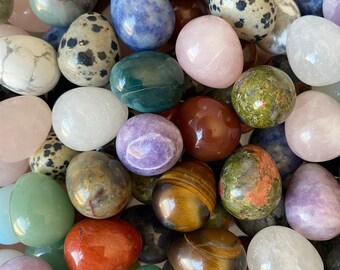 Puede incluir: Una colección de huevos de piedras preciosas pulidas en varios colores y patrones. Los huevos incluyen tonos de rosa, verde, marrón, azul y blanco, con texturas moteadas y veteadas. Las piedras preciosas están dispuestas juntas, llenando el marco.