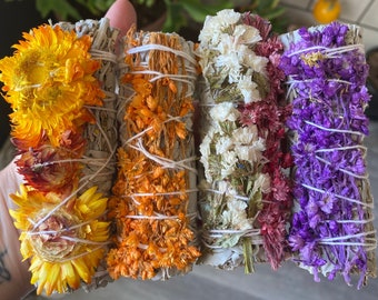 May include: Four bundles of dried sage, each adorned with different colored dried flowers. The flowers include yellow, orange, white, red, and purple. The sage bundles are tied with white twine.