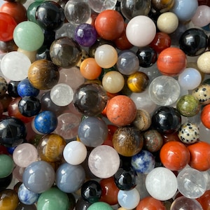 May include: A collection of various gemstone spheres in a variety of colors, including red, green, black, and clear. The spheres are of different sizes and textures, creating a visually diverse display. The gemstones appear to be polished and smooth.