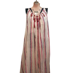 Puede incluir: Un vestido largo y fluido con rayas verticales en crema, rojo y azul marino. El vestido presenta un escote en V con cord&oacute;n y borlas decorativas. La prenda es sin mangas y parece estar hecha de una tela ligera.