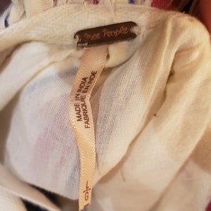 Puede incluir: Primer plano de tela color crema con rayas rojas y azules. Una etiqueta marr&oacute;n dice "Free People". Una etiqueta crema dice "MADE IN INDIA FABRIQUE EN INDE" con talla "L/G."