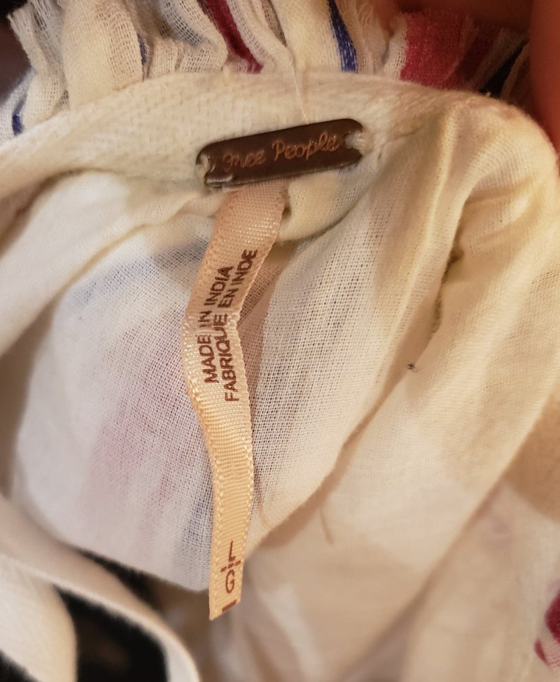 Puede incluir: Primer plano de tela color crema con rayas rojas y azules. Una etiqueta marr&oacute;n dice "Free People". Una etiqueta crema dice "MADE IN INDIA FABRIQUE EN INDE" con talla "L/G."