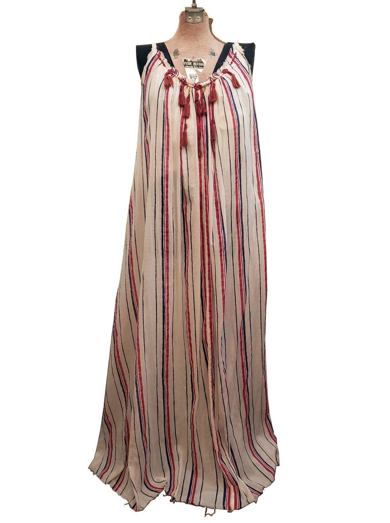 Puede incluir: Un vestido largo y fluido con rayas verticales en crema, rojo y azul marino. El vestido presenta un escote en V con cord&oacute;n y borlas decorativas. La prenda es sin mangas y parece estar hecha de una tela ligera.
