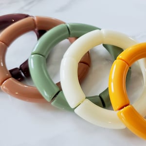 May include: Six colorful bracelets made of chunky plastic beads. The bracelets are in shades of brown, green, white, yellow, and pink.
