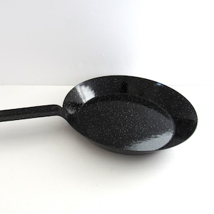 May include: A black speckled enamel frying pan with a long handle. The pan has a rounded shape and a speckled pattern. The handle has a hole at the end for hanging. Kitchenware.