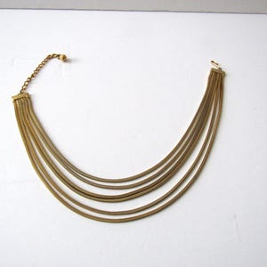 May include: A gold-toned necklace with multiple strands. The necklace features a series of thin, parallel chains that cascade downwards. The clasp and chain are visible at the top, and the necklace is set against a white background.