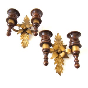 May include: A pair of gold metal wall sconces with a floral design. Each sconce has two wooden candle holders.
