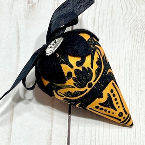 May include: A cone-shaped ornament with a black ribbon and a small silver charm. The ornament is black and gold with a decorative pattern. The ribbon is tied in a bow at the top. The ornament is likely for Halloween or a similar holiday.