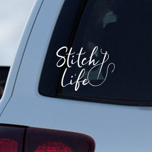 May include: White vinyl decal with the words "Stitch Life" in a cursive font. The decal is applied to the window of a vehicle. The design includes a needle and thread, suggesting a crafting theme.