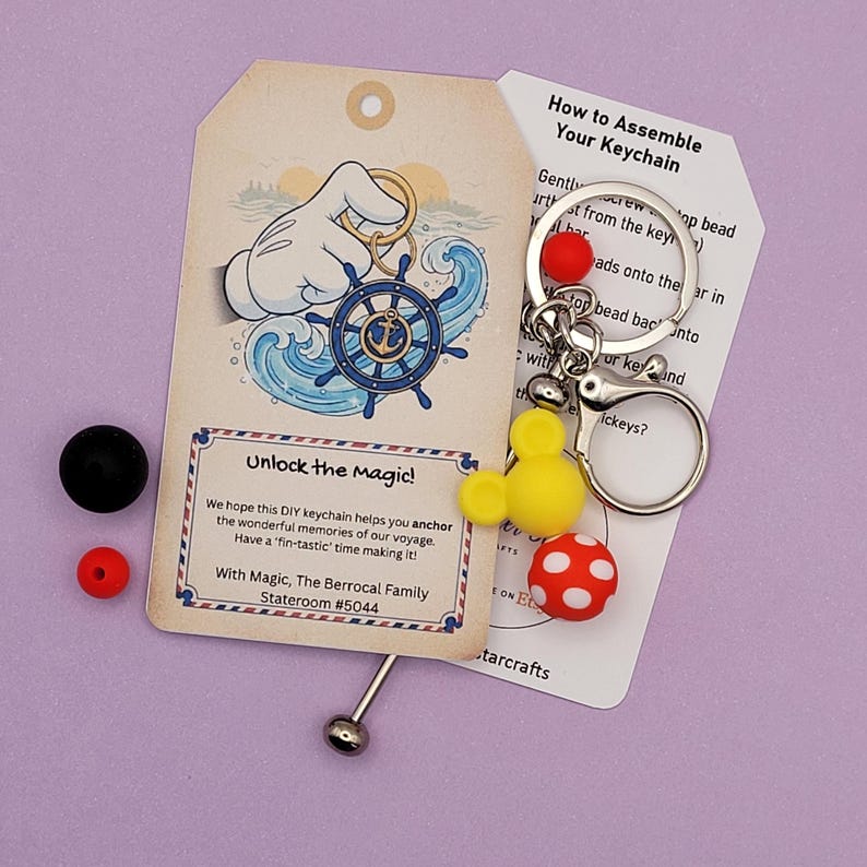 May include: DIY keychain kit with a nautical theme. Includes a tag with a Mickey Mouse hand holding a ship's wheel, a yellow Mickey Mouse head, a red polka dot bead, and a red bead. The tag reads "Unlock the magic!"