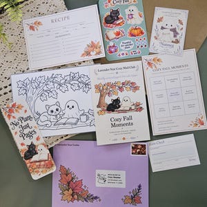 May include: A collection of stationery items featuring autumn themes, including a recipe card, a sticker sheet with a black cat and ghost, a coloring page, a bookmark with the text No Plans Just Pages, a Lavender Star Cozy Mail Club card, and a purple envelope.