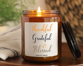 May include: A brown glass candle jar with a white label that reads "Thankful Grateful & Blessed" and "Home of Thrace". The candle is lit and the flame is visible.