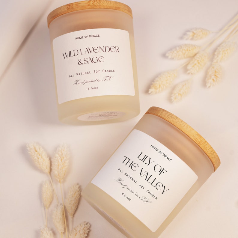 K&ouml;nnte beinhalten: Zwei gefrostete Glaskerzenbeh&auml;lter mit Holzdeckeln. Die Beh&auml;lter sind mit einem hellgelben Kerzenwachs gef&uuml;llt. Die Etiketten auf den Beh&auml;ltern lauten "Wild Lavender & Sage" und "Lily of the Valley". Beide Kerzen sind reine nat&uuml;rliche Sojawachskerzen und werden in Texas handgegossen. Jede Kerze wiegt 8 Unzen.