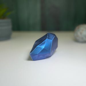 Puede incluir: Un pisapapeles de cristal azul facetado y geom&eacute;trico. El cristal tiene un acabado brillante e iridiscente.