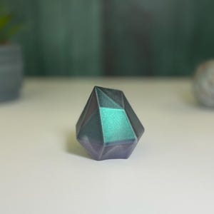 Puede incluir: Un pisapapeles de cristal geom&eacute;trico, facetado, iridiscente en color verde azulado y morado.