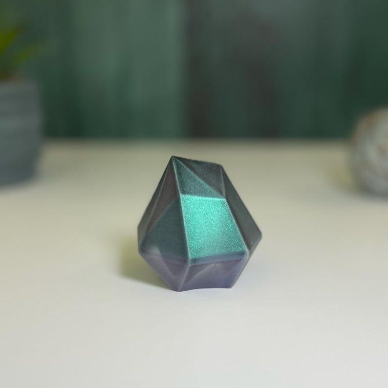 Puede incluir: Un pisapapeles de cristal geom&eacute;trico, facetado, iridiscente en color verde azulado y morado.