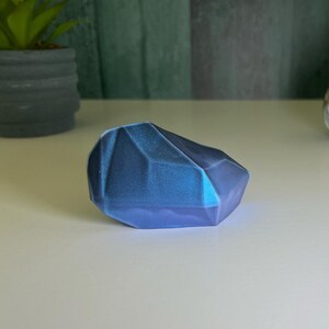 Puede incluir: Una roca de forma geom&eacute;trica azul y morada con un acabado brillante.