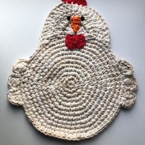 May include: A crocheted white chicken-shaped coaster with red and orange details. The coaster has a round centre and a scalloped edge.