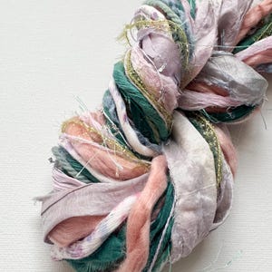 May include: A skein of yarn with a mix of pink, green and white ribbons. The yarn is soft and fluffy, and the ribbons are delicate and flowing.