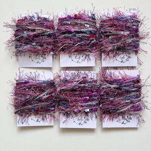 May include: Six spools of purple, pink and blue yarn with a white label that says "Everything Looks Lovely" on each spool.