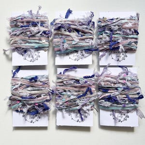 May include: Six spools of colorful, shredded fabric ribbon in shades of pink, blue, and white. Each spool is wrapped in white cardstock with the words "Three Little Birds" printed in black.