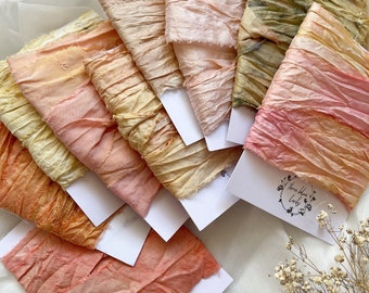 May include: A collection of colorful, textured fabric ribbons in shades of yellow, peach, pink, and olive green. Each ribbon is mounted on a white card. The ribbons have a crinkled, raw-edged appearance, suggesting a handmade or artisanal quality.