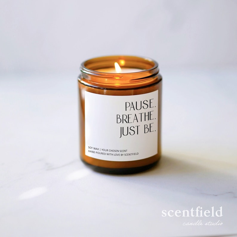 May include: A brown glass candle jar with a white label that reads "PAUSE. BREATHE. JUST BE." Soy wax candle with your chosen scent. Hand poured with love by Scentfield.