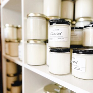 May include: A shelf display of white scented candles in glass jars with black lids. The candles are labeled "Coastal" and "Scentfield" with the scent "Orange Citrus & Cedarwood". The candles are 4 oz / 113 g and handmade in Texas.