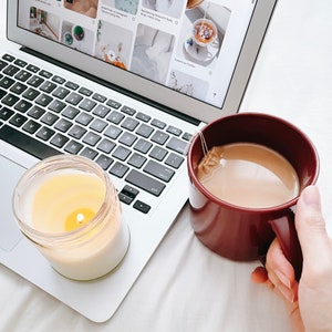 May include: A close-up of a laptop computer with a lit candle and a mug of tea. The laptop screen shows a Pinterest page with images of home decor and DIY projects.