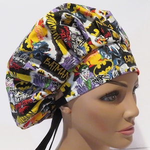 Puede incluir: Un gorro de quirófano negro y amarillo con un estampado de cómic de Batman que presenta los logotipos de Joker y Batman. El gorro tiene lazos negros.