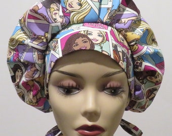 May include: A pink and blue patterned surgical cap with a tie. The pattern features images of dolls with the text "Born to Lead", "Girl Strong", and "I Can Do It" on the cap.