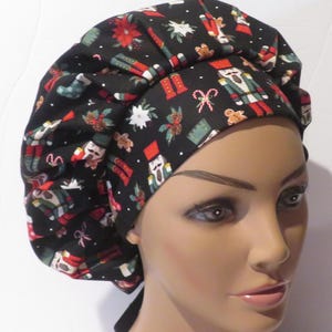 May include: A black bouffant scrub cap with a Christmas-themed design. The cap displays images of nutcrackers, gingerbread men, candy canes, and poinsettias in red, green, and white. The cap is designed to cover the hair during medical procedures.