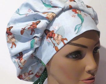 May include: A light blue surgical scrub hat featuring a repeating pattern of cartoon characters and mermaids. The hat has a green and white polka dot tie. The hat is designed to cover the hair.