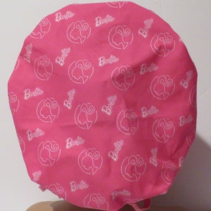 May include: Pink fabric shower cap with a white outline of a woman's face and the word "Barbie" repeated throughout.