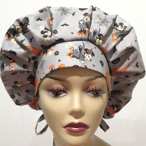 May include: Gray and orange scrub hat with a Halloween Mickey Mouse print. The hat has a gathered top and ties at the back.