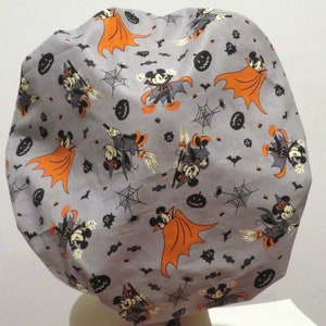May include: A gray fabric shower cap with a Halloween theme featuring Mickey Mouse and Minnie Mouse dressed as a vampire and a witch. The cap is covered in a repeating pattern of Mickey and Minnie, bats, pumpkins, candy corn, and spiderwebs.