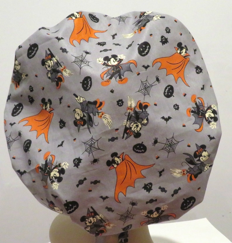 May include: A gray fabric shower cap with a Halloween theme featuring Mickey Mouse and Minnie Mouse dressed as a vampire and a witch. The cap is covered in a repeating pattern of Mickey and Minnie, bats, pumpkins, candy corn, and spiderwebs.