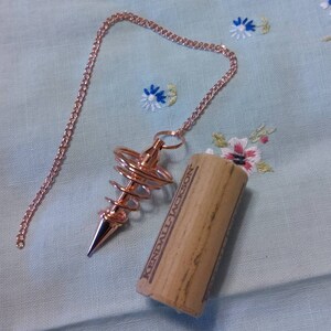 Peut inclure: Un pendule en métal de couleur or rose avec un design en spirale suspendu à une chaîne. Le pendule repose sur un bouchon de liège sur lequel est imprimé le texte "KENDALL JACKSON".