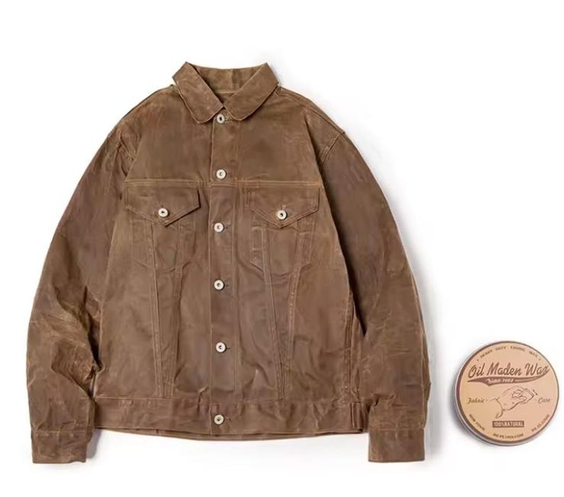 May include: A brown, button-up jacket with two chest pockets and two side pockets. The jacket has a classic collar and is made of a waxed material. A round tin of "Oil Maden Wax" is next to the jacket.
