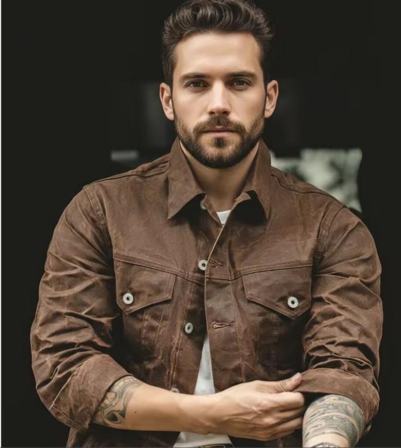 May include: A brown jacket with two chest pockets and button fastenings. The jacket has a collared neckline and is worn over a white shirt. The sleeves are long and buttoned at the cuffs. The jacket appears to be made of a durable material.