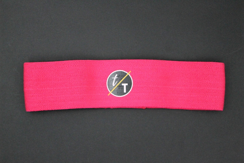 Puede incluir: Banda de resistencia de tela rosa con un logotipo circular negro que dice "t/T".