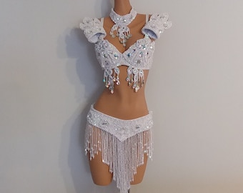 May include: White beaded costume set with a bra, skirt, and matching necklace. The bra and skirt are embellished with iridescent sequins and the skirt has a fringe trim.