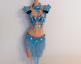 May include: A turquoise belly dance costume with intricate beadwork and fringe. The set includes a bra, arm cuffs, a choker, and a skirt. The costume is displayed on a mannequin against a white background.