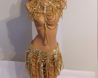 Pode incluir: Conjunto de fantasia de contas douradas com uma coroa, um colar e uma saia. A coroa tem um design de raios de sol com strass dourados e transparentes. O colar é um design em camadas com contas douradas e strass transparentes. A saia é um design em camadas com contas douradas e strass transparentes.