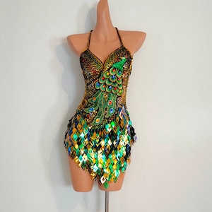 May include: A gold and green sequined dress with a peacock design. The dress has a halter neckline and a short skirt.