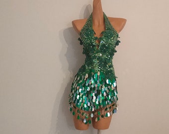 May include: A green sequined halter top with a short skirt. The top has a V-neckline and is adorned with green sequins. The skirt is also made of green sequins and has a fringe hem.