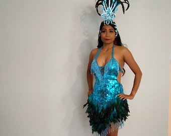 May include: A woman wearing a blue sequined dress with a green feather trim and a sparkling headpiece. She is wearing red heels.