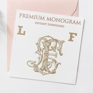May include: A white card with a gold monogram design featuring the letters "L" and "F". The card also has the text "PREMIUM MONOGRAM" and "INSTANT DOWNLOAD" in gold. The card is placed on a white surface with a pink envelope.