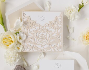 May include: A white and cream wedding invitation with a laser cut floral design. The invitation features the initials "E & J" and the date "18.08.2023". The RSVP card includes the date "1st July 2023".